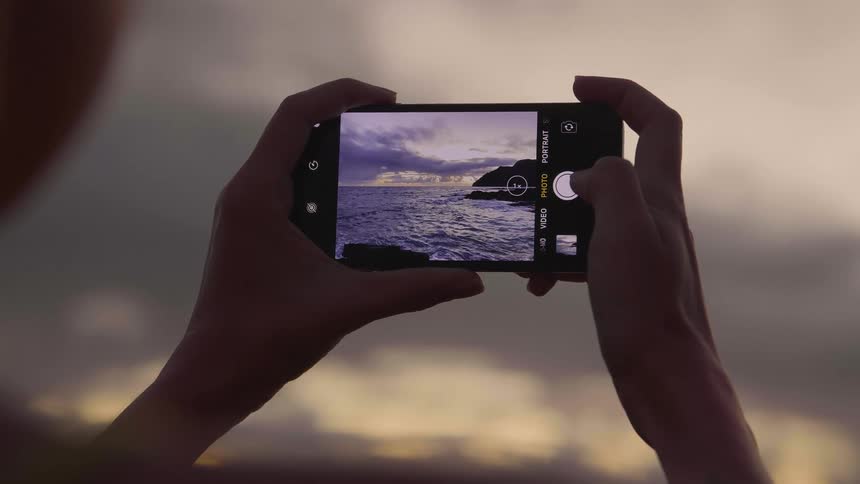 Woman takes photographs of the sea and the promontory overlooking the bay at dusk