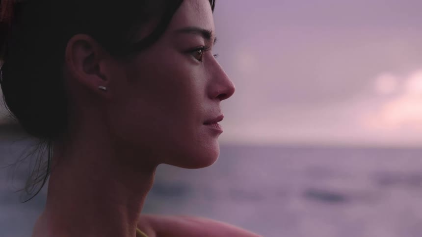 Side view of a woman with earrings taking photographs of the sea at dusk