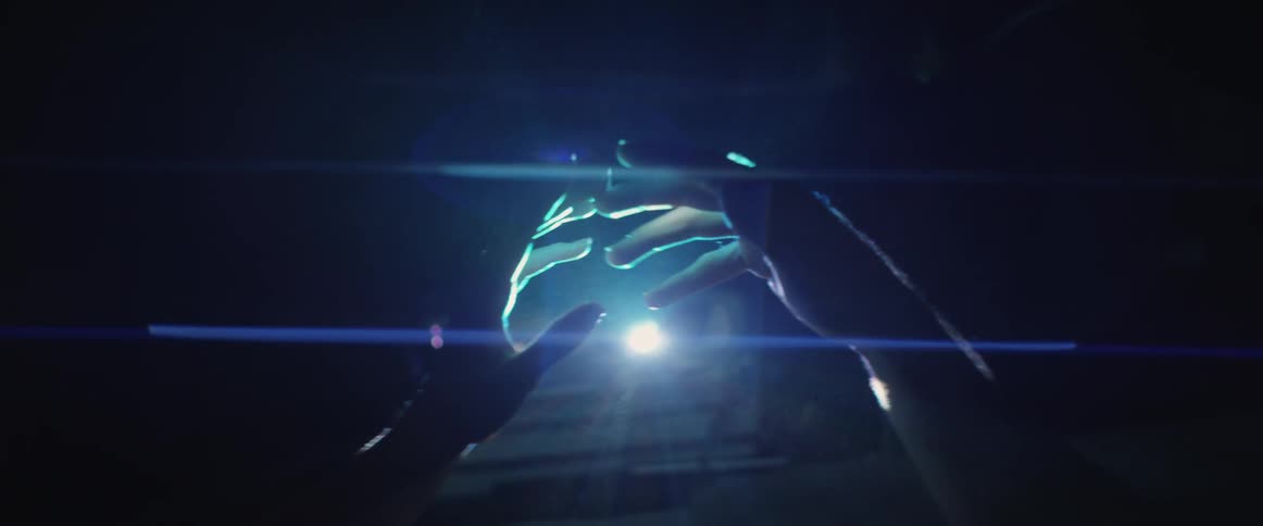 Two folded hands unclasp in front of a single light at night