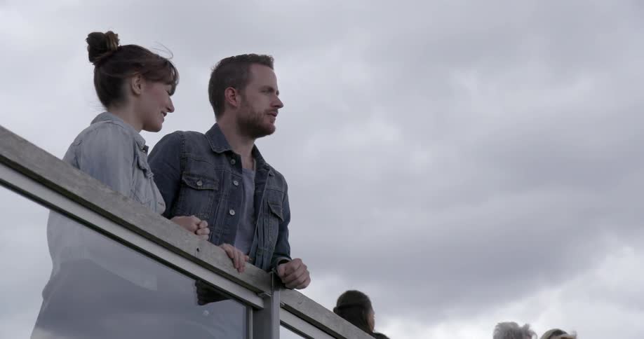 A man and woman lean against a railing and talk