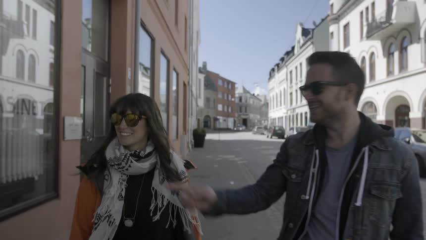 A man and woman walk down a street in front of buildings