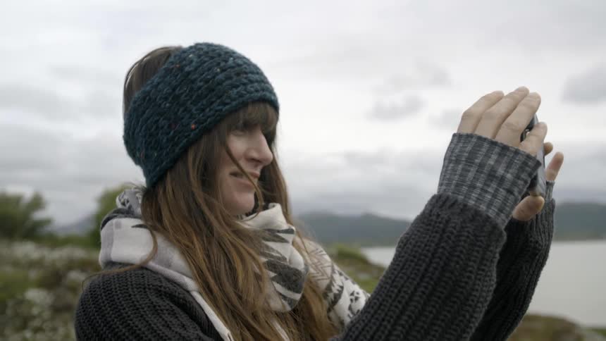 A woman is smiling as she films with a phone