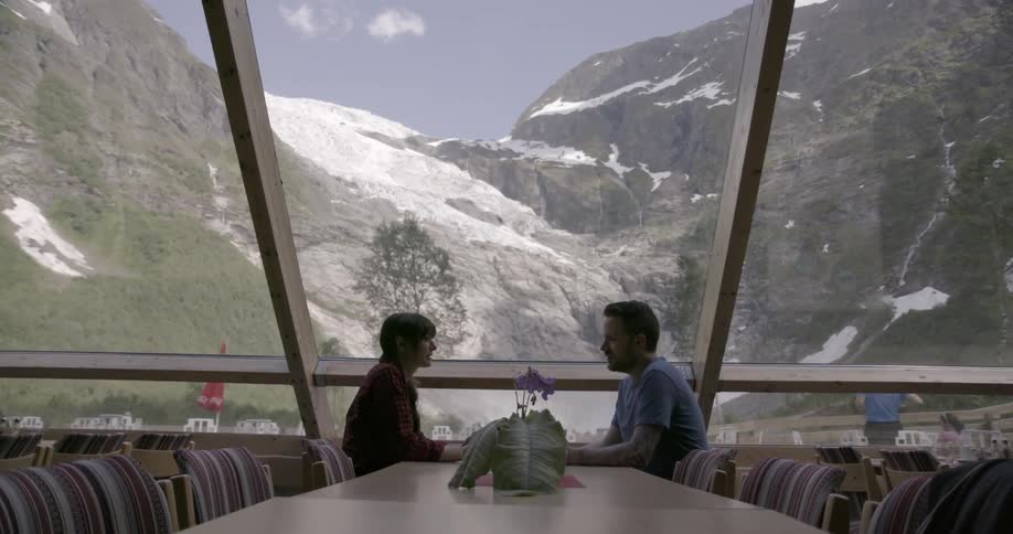 A man and woman sit at a restaurant table with a mountain view