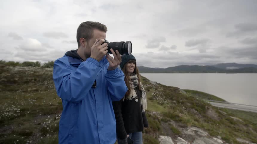 A man takes pictures of a body of water while a woman smiles