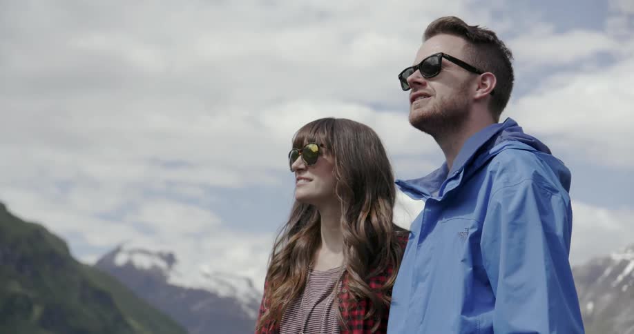 A man and woman are standing outside wearing sunglasses
