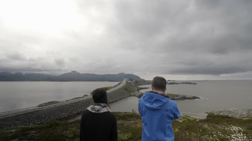 Two people are standing by a lake on a cloudy day