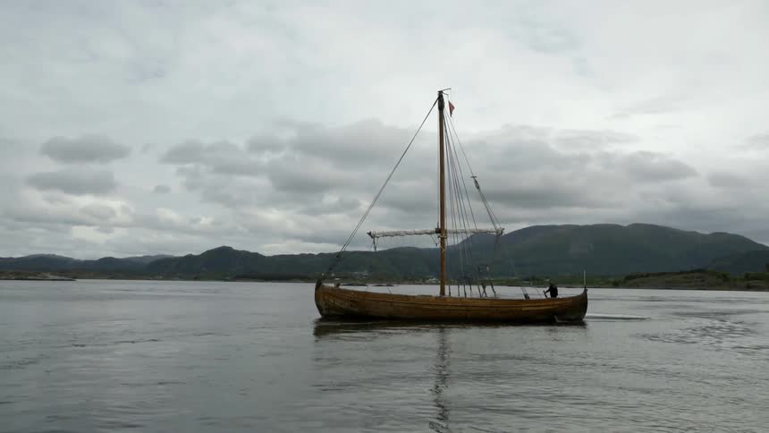 A boat floats along a lake on a cloudy day