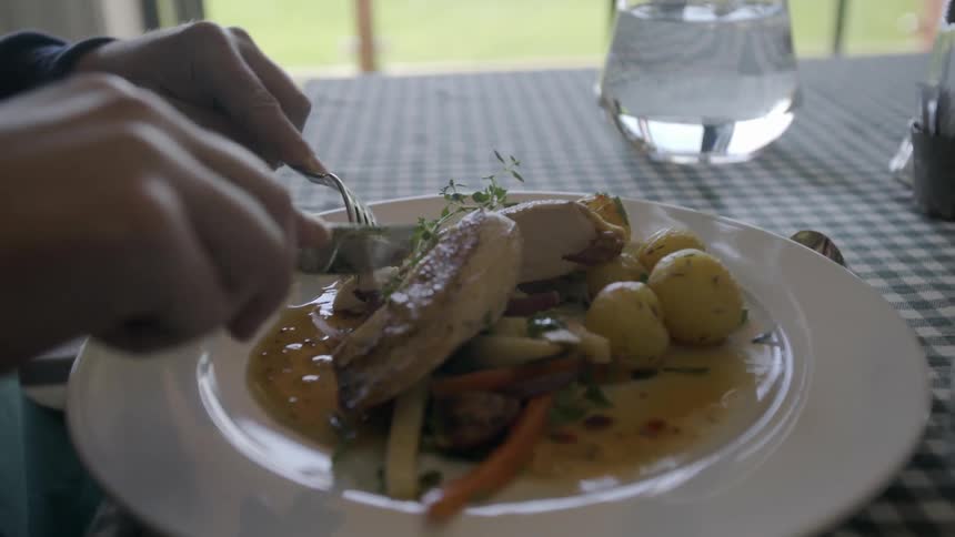 A person is cutting his food and takes a bite with a fork