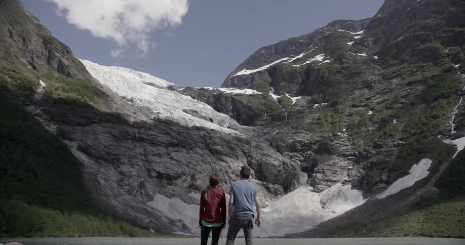 A man and woman stand in front of a lake and look at a mountain