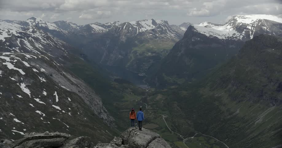 A man and woman stand on a rock looking out at a massive valley.\