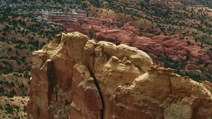 A red rocky mountain plateau stands tall in a wide open hills filled valley scattered with green vegetation