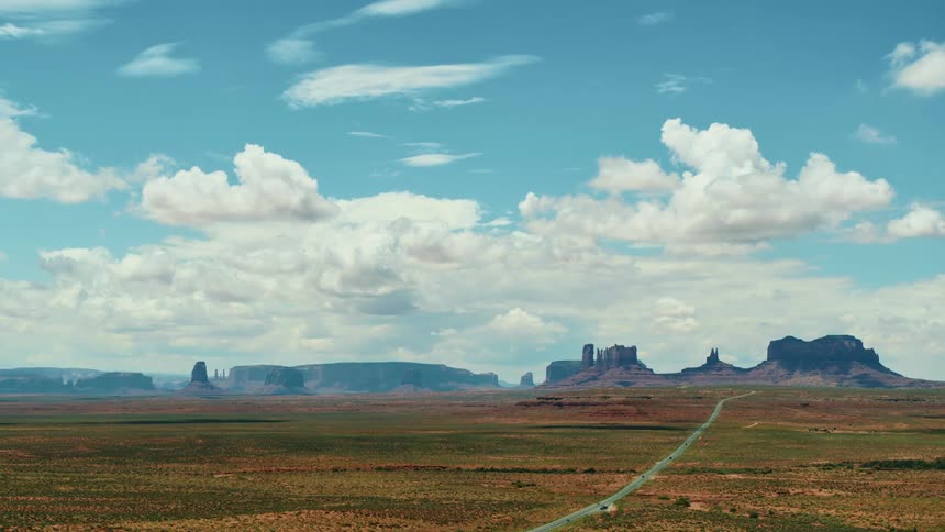 A desert with a road with plateaus cliffs the sky and clouds in the background