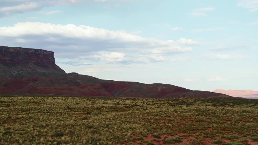 A grassy red dirt open plain spans through a rocky mountainous area