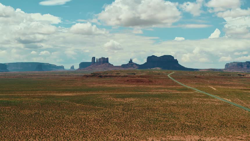 A narrow curvy road runs through a vast field and leads to mesa formations