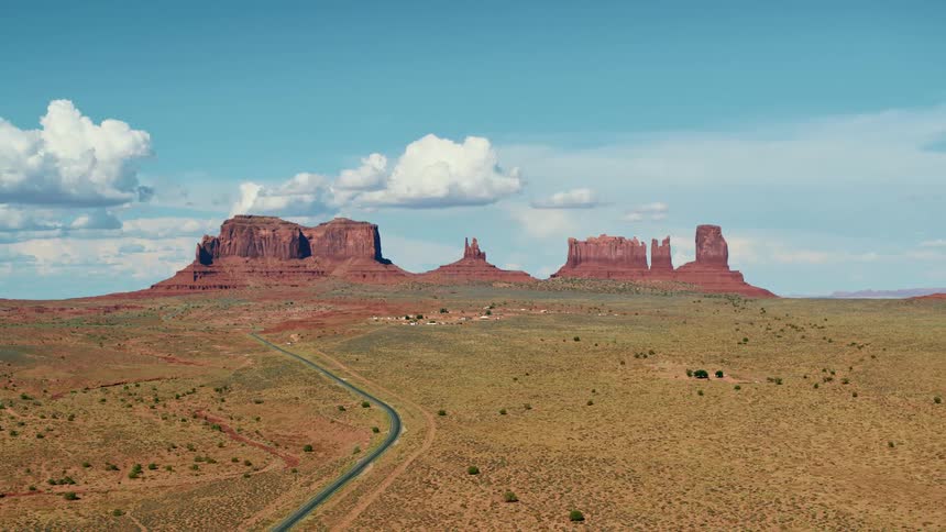A curved road through a vast field leads to a mesa formation