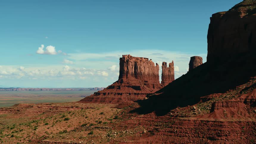 Plainsand desert stretch past mesa and buttes under slightly cloudy blue sky