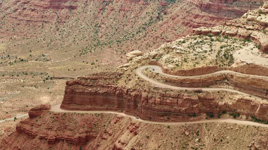 An aerial view of a car driving on a cliffside road in a rocky desert canyon