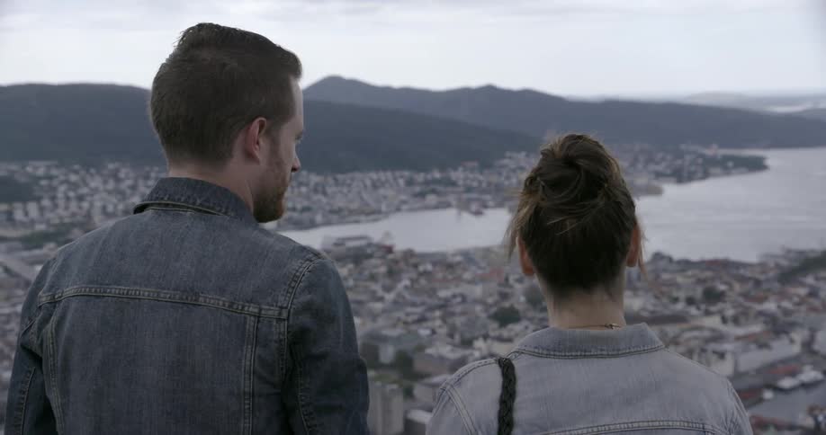A man and woman stand overlooking a lakeside city