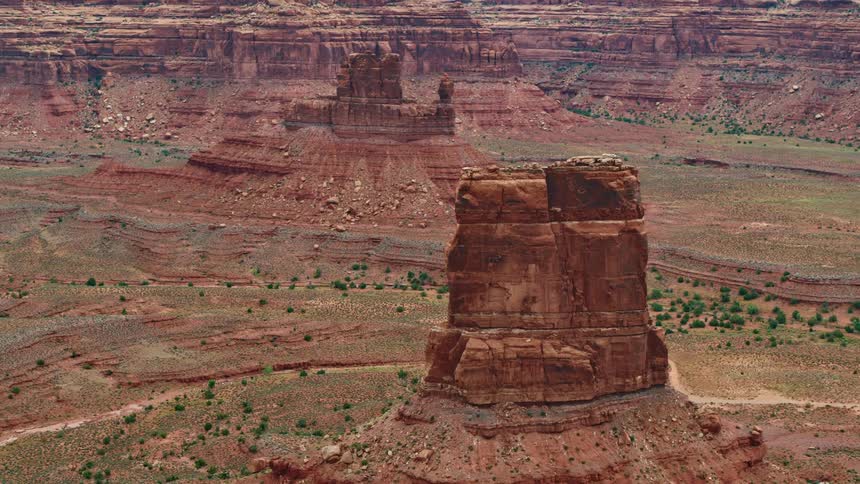 Red rocks rise from the ground surrounded by layers of rock and shrub
