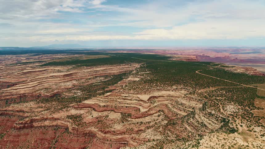 Road cuts through striated terrain covered in vegetation near canyon edge