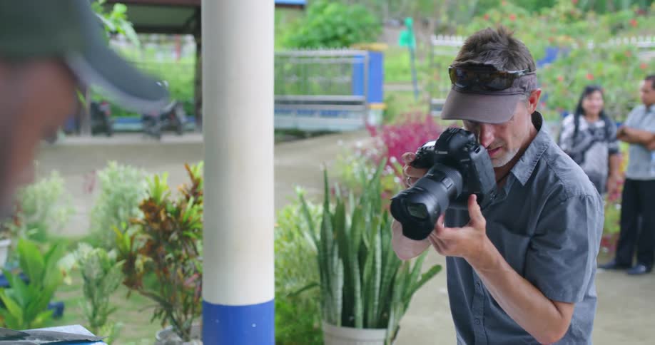 A man takes photos of shark fins in a village as people stand in the background