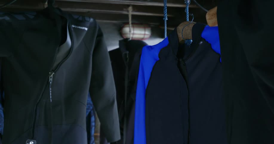 Jackets and wet suits hang from a ceiling display made of silver pipes