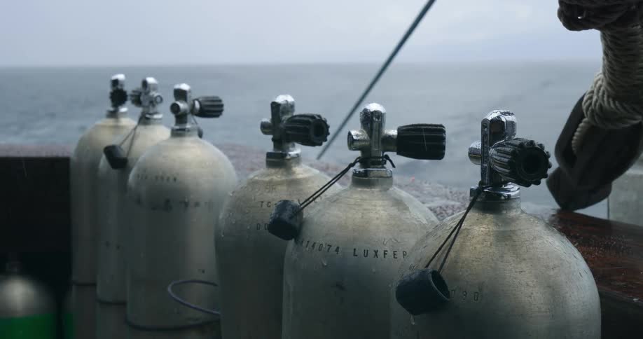 Row of scuba tanks sit on boat near rope as waves stretch to horizon