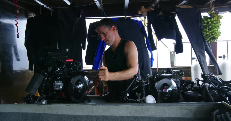 A man works on parts of a motorcycle in a carport as laundry is hung to dry behind him