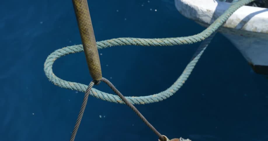 Barefoot person standing in boat tugs onmooring line undoing knot causing rope to fall into water