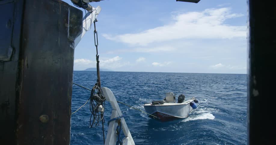 A boat tied with a rope in the ocean with the sky and clouds in the background