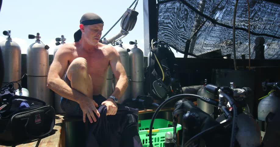 A man surrounded by oxygen tanks puts on a wet suit