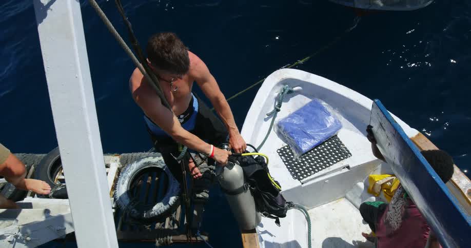 A group of men load diving equipment onto a board on a sunny day
