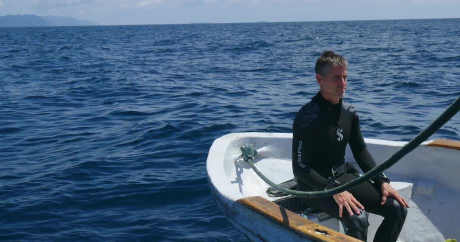 A man is sitting on a boat in the middle of the ocean