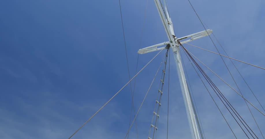Several cables and wires are attached to the mast of a sailboat