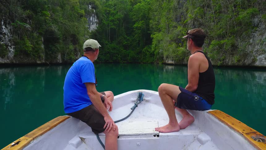 Two men sit on a boat as it drifts to the shore