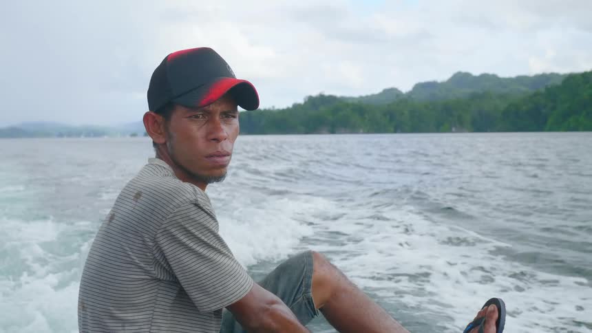 A man rides a boat along the coast of landmass covered in thick forest