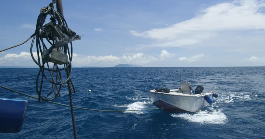 A motorboat is towed via towing cable across the ocean by a larger vessel