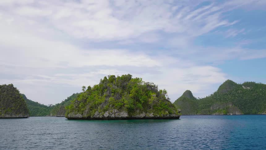 An island with trees surrounded by water with land the sky and clouds in the background