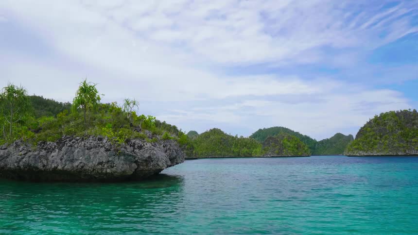 A islet off the coast of a larger landmass on the bluegreen waters of the ocean on a sunny day