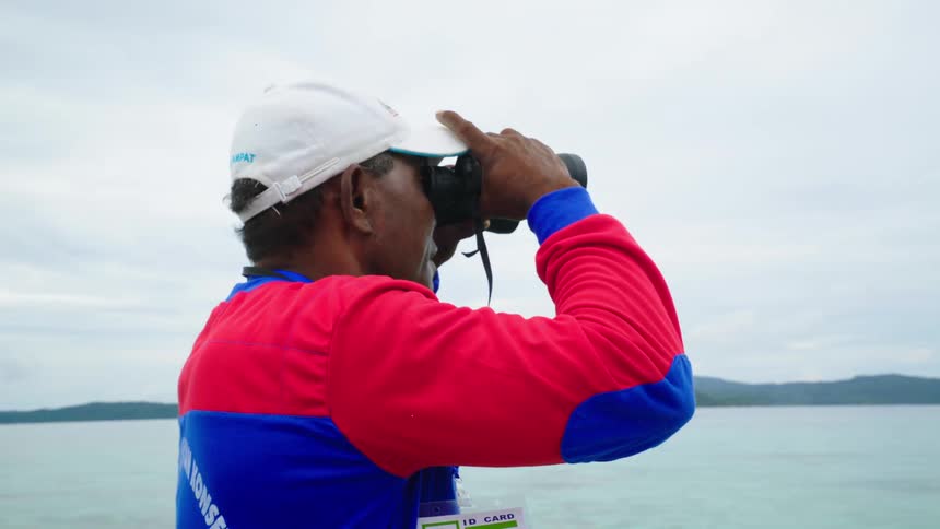 A ranger looks out over the ocean with a pair of binoculars during the day