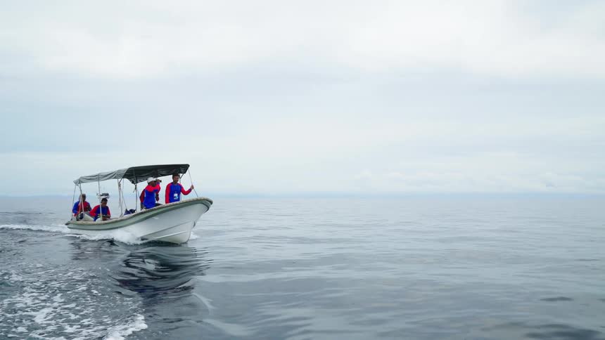 A group of men in matching jackets ride a boat across the ocean during the day
