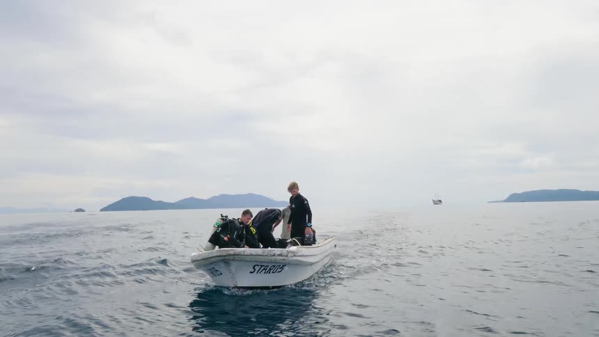 Divers prepare their equipment for a dive while riding on the ocean on a small boat on a cloudy day