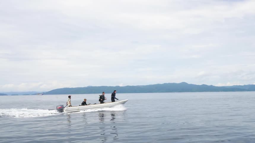 Four men on a boat with land the sky and clouds in the background