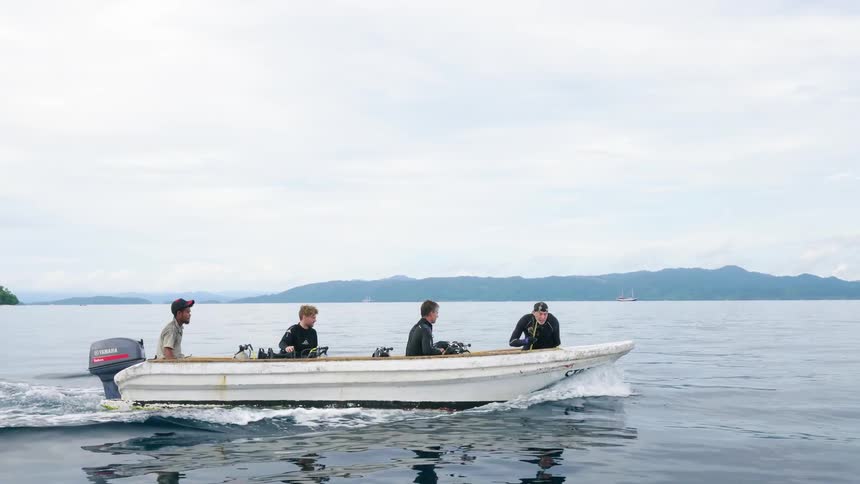 Men in diving gear assemble equipment on a boat as it glides across the ocean