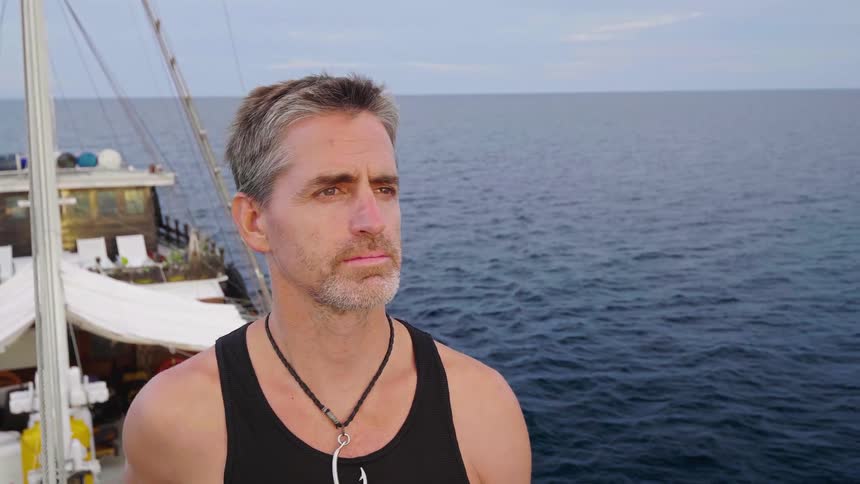 A man looks out over the ocean while standing on the bow of a boat