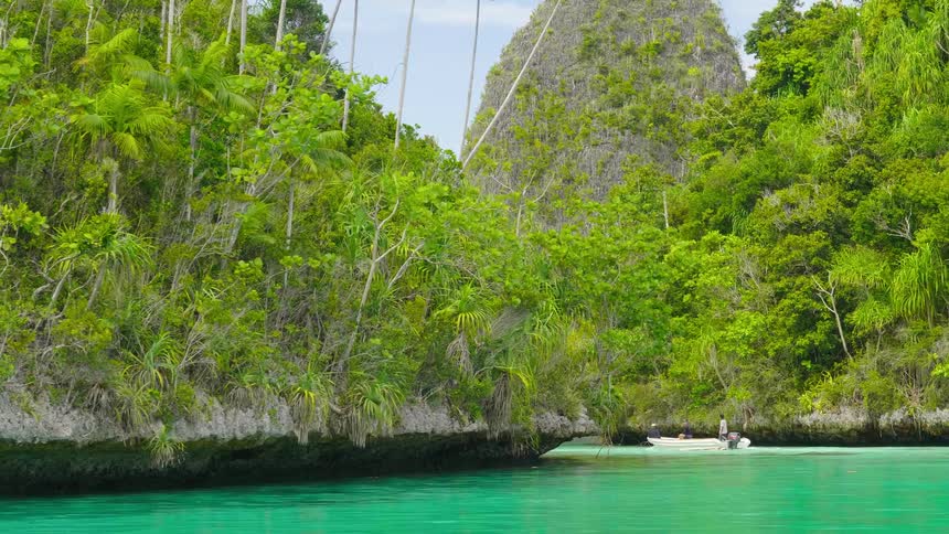 Three people sail on a boat past islands