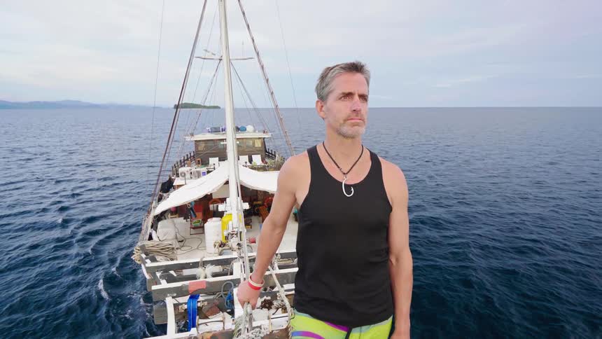 A man stands on the bow of a boat as it travels across the ocean