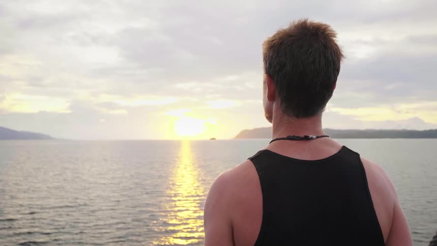 A middle aged man looks out over the ocean towards the low sun while standing on a boat