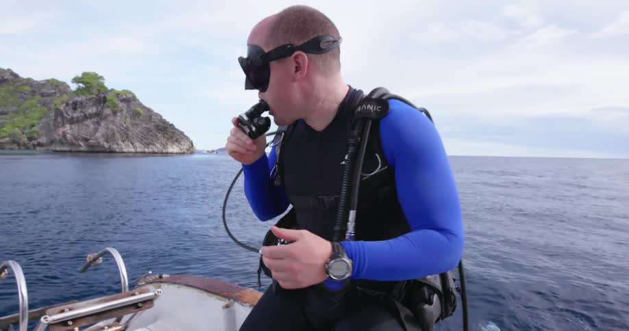 A man wearing scuba gear flips backwards off of a boat into the water