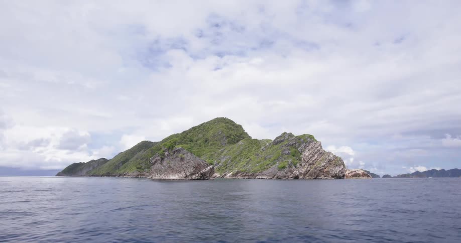 An island in the ocean with land the sky and clouds in the background